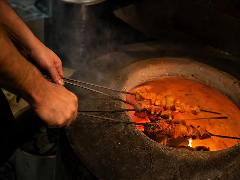 Skewers of chicken tikka going into a glowing clay tandoor oven.
